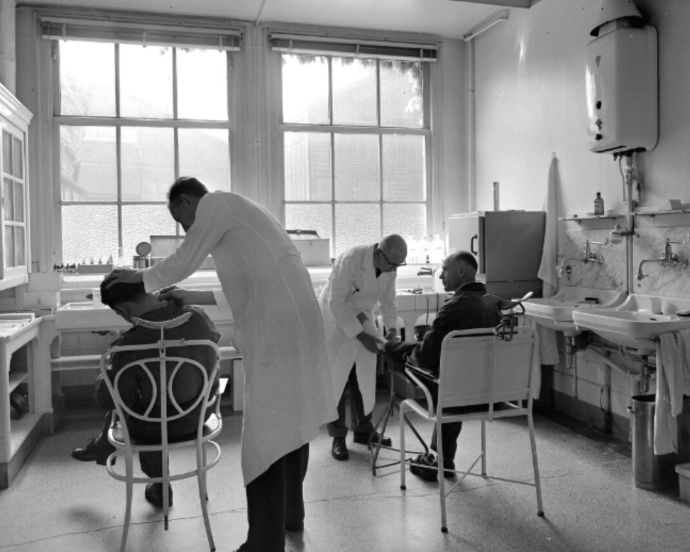 1962 Interieur van de oude verbandkamer, artsen onderzoeken werknemers.